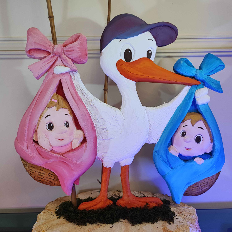 در این تصویر یک دکور جذاب برای تعیین جنسیت نوزاد دیده میشود. لکلکی در مرکز تصویر قرار دارد که در دو طرف خود سبدهایی با نوزاد دارد؛ یکی با روبان صورتی برای دختر و دیگری با روبان آبی برای پسر.