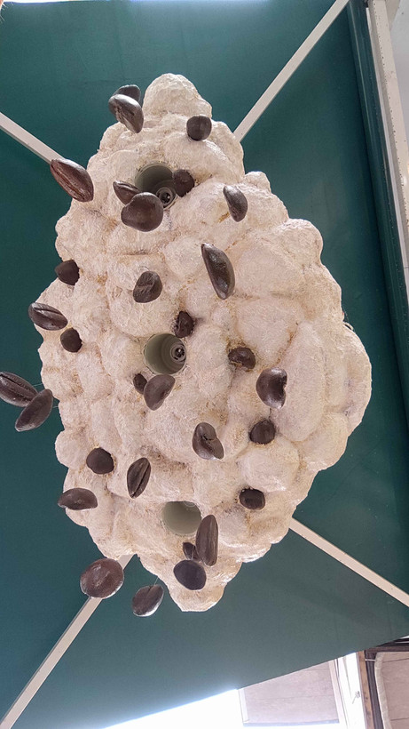 اثر تزئینی دیواری با طراحی ابر، همراه آویز دانههای قهوه؛ نصبشده در فضای گرم کافه، مناسب برای فضاسازی احساسی و مینیمال