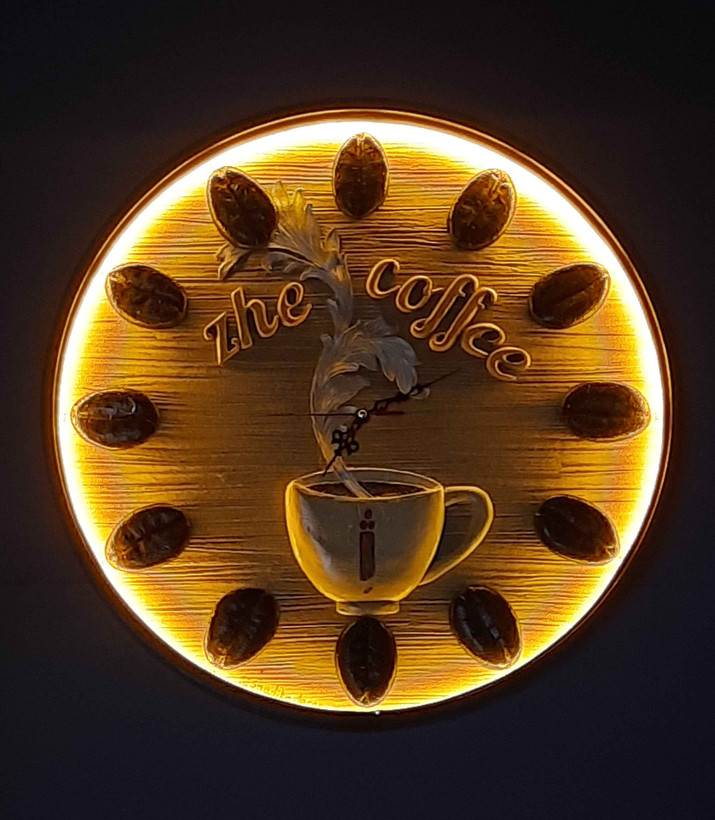 ساعت دیواری چوبی با طراحی خاص برای کافه ژ، شامل چیدمان دانههای قهوه به جای اعداد ساعت، تصویر فنجانی با بخار در حال بالا رفتن در مرکز، و عناصر گرافیکی مینیمال با رنگهای گرم؛ القاکنندهی فضایی دنج و صمیمی