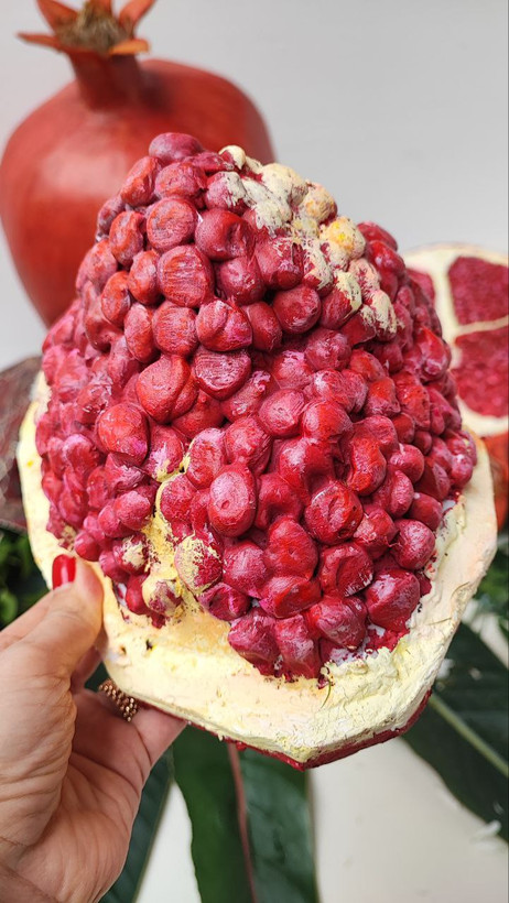 ماکتهای انار برشخورده با دانههای طبیعینما، چیدهشده روی پارچه سنتی با گل و برگ؛ مناسب برای دکور شب یلدا و ویترین فرهنگی