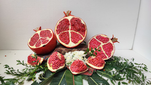 ماکتهای انار نصفه و برشخورده با دانههای طبیعینما، چیدهشده روی پارچه سنتی با گل و برگ؛ مناسب برای دکور شب یلدا و ویترین فرهنگی