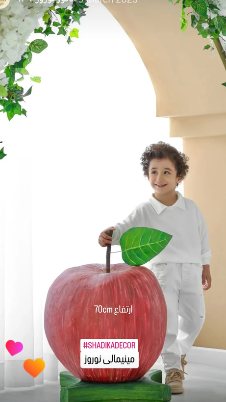 ماکت سیب 70 سانتی در کنار کودکی در اتلیه عکاسی کودک برای دکور نوروزی